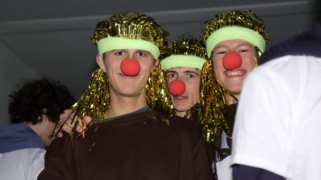 Eerstejaars met clownsneuzen en glitterpruiken tijdens de doop